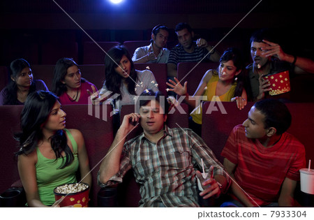 Man talking on a mobile phone in a cinema hall 7933304