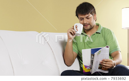 Man reading a magazine while drinking coffee 7933692