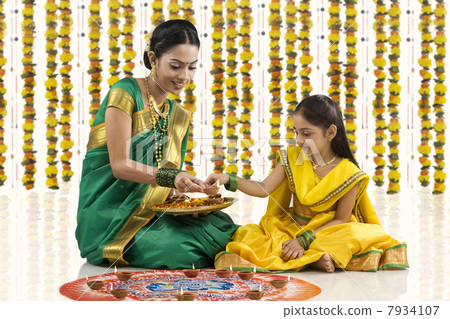 Mother and daughter placing diyas on a rangoli Mother and daughter placing diyas on a rangoli 7934107