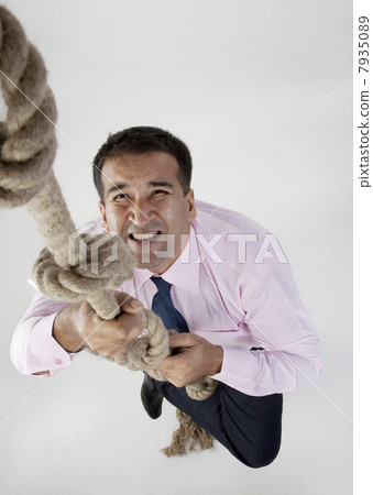 Businessman trying to climb a rope 7935089