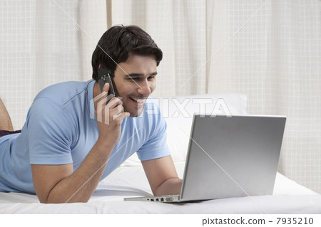 Man talking on the phone while working on a laptop 7935210