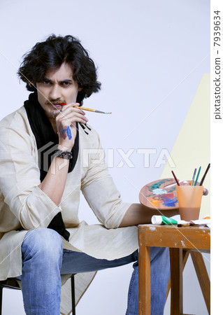 Portrait of handsome male artist with palette and paintbrush against colored background 7939634