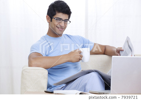 Young man enjoying cup of coffee at home while looking at laptop 7939721