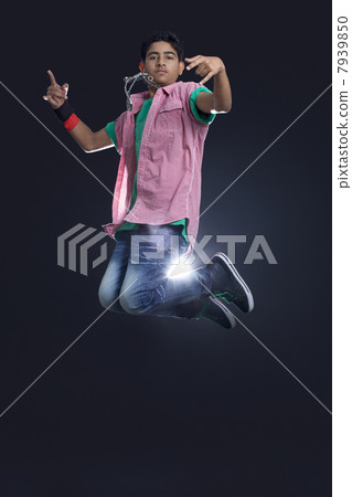 Funky teenage boy jumping in air showing rock and roll sign against black background 7939850