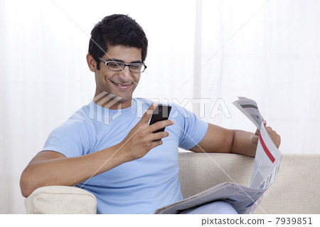 Happy young man looking at mobile phone while sitting on sofa 7939851
