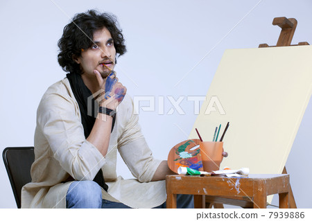 Young male artist contemplating near easel against colored background 7939886