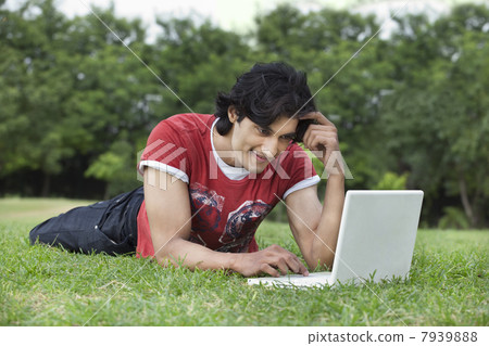 Smiling young man lying on grass using laptop 7939888