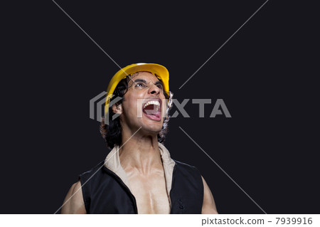 Close-up of young man with hardhat shouting against black background 7939916