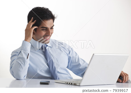 Happy young male executive smiling while looking at laptop 7939917