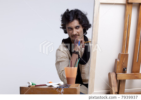 Young male artist looking at painting against colored background 7939937