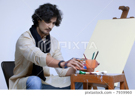 Young artist sitting near easel against colored background 7939960