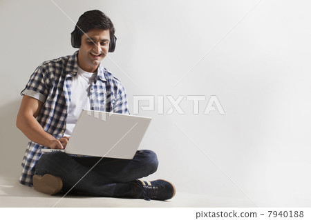 Man wearing headphones and using laptop Man wearing headphones and using laptop 7940188