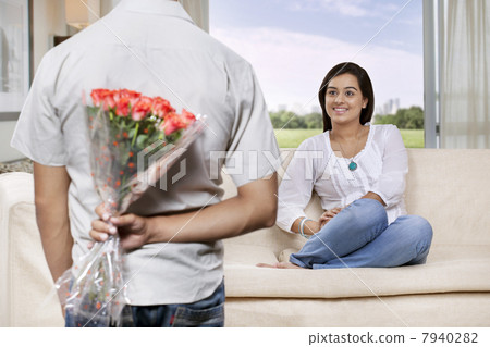 Man hiding bunch of flowers behind back while woman watching 7940282