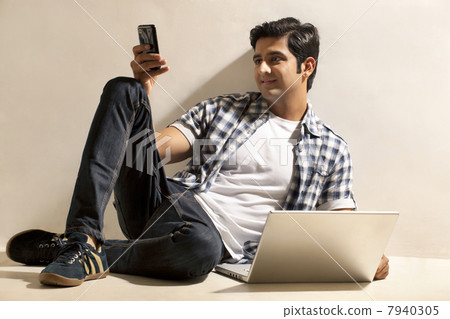 Happy relaxed young man sitting by laptop while reading text message Happy relaxed young man sitting by laptop while reading text message 7940305