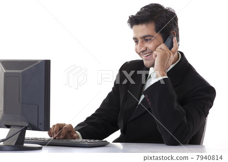 Happy smart businessman working on computer while talking on cell phone Happy smart businessman working on computer while talking on cell phone 7940814