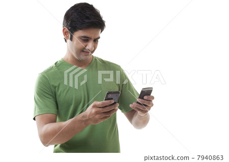 Smart young man text messaging through cell phones over white background 7940863