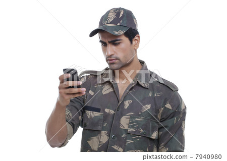 Serious young soldier reading message on his cell phone 7940980