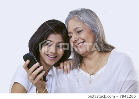 Close-up of a mature woman and her granddaughter looking at a mobile phone and smiling 7941206