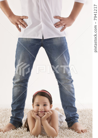 Portrait of daughter lying between fathers legs on rug 7941217