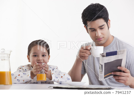 Little girl drinking juice while father reading newspaper 7941237