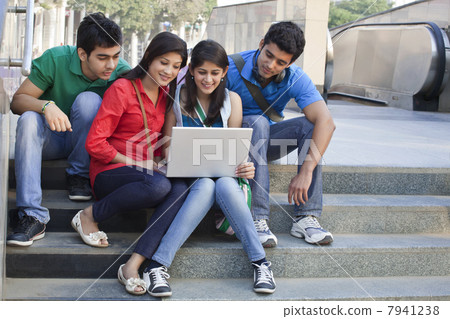 Group of friends using laptop while sitting on steps 7941238