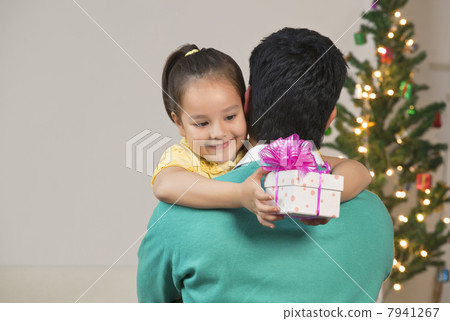 Smiling girl hugging her dad while holding Christmas gift 7941267