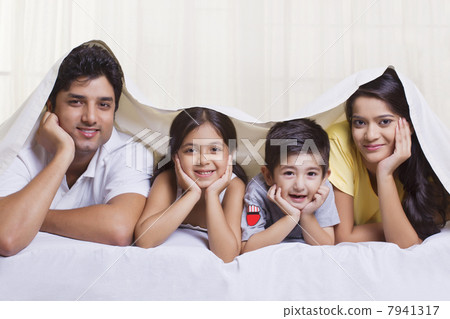 Portrait of parents with children lying under bed cover Portrait of parents with children lying under bed cover 7941317