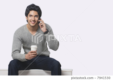 Young man talking on cell phone while holding disposable cup 7941530