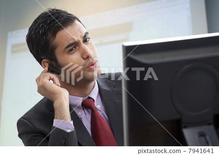 Smart male executive looking at computer while conversing on call 7941641