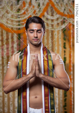 Handsome groom praying with garlands hanging in background 7942311