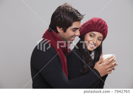 Smiling young couple holding cup over grey background Smiling young couple holding cup over grey background 7942765