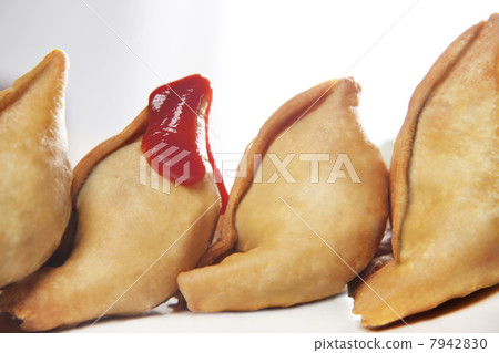 Ketchup sauce on samosas kept in row over white background 7942830