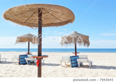 Sunny beach in Portugal with wooden umbrellas near the sea. Summ Sunny beach in Portugal with wooden umbrellas near the sea. Summ 7943645