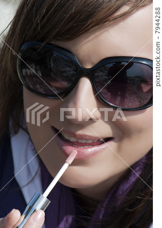 Beautiful brunette applies lip gloss 7944288
