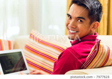 Asian man sitting on couch surfing the internet Asian man sitting on couch surfing the internet 7977628
