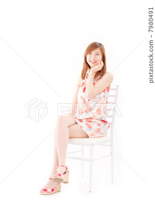 一個漂亮的女孩在她二十多歲坐在白色的椅子上，笑著用她的雙手在她的臉頰上 7980491