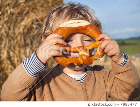 Lovely little boy of two years with pretzel on hay field 7985477