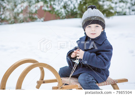 Lovely little boy on ancient sledge on winter day Lovely little boy on ancient sledge on winter day 7985504
