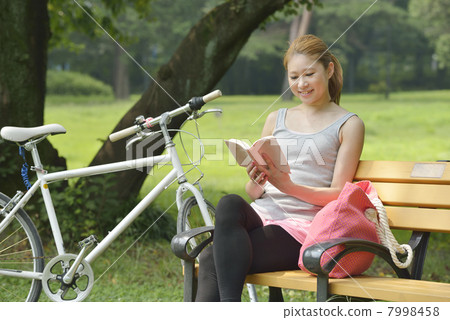 A young woman reading a book on a park bench A young woman reading a book on a park bench 7998458