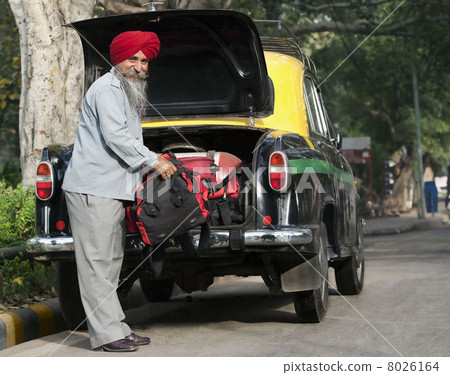 Sikh taxi driver loading luggage into the dickie Sikh taxi driver loading luggage into the dickie 8026164