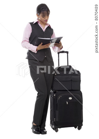 Full length of beautiful businesswoman with luggage reading book 8070489