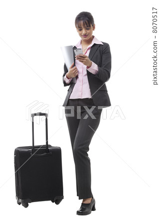 Full length of a young businesswoman with luggage reading text message Full length of a young businesswoman with luggage reading text message 8070517