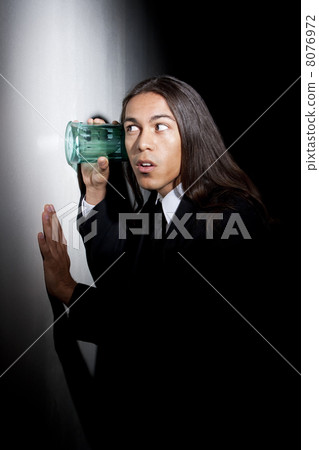Handsome young mixed race man using glass to eavesdrop 8076972
