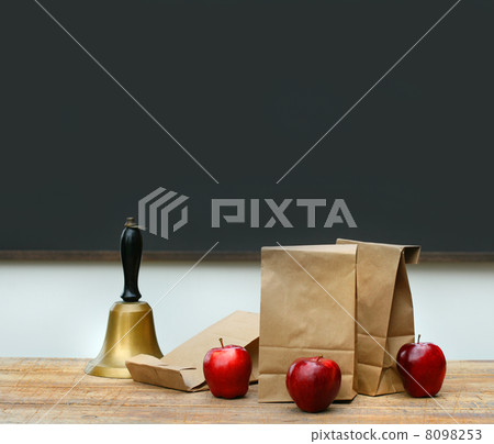 Lunch bags with apples and school bell on desk 8098253
