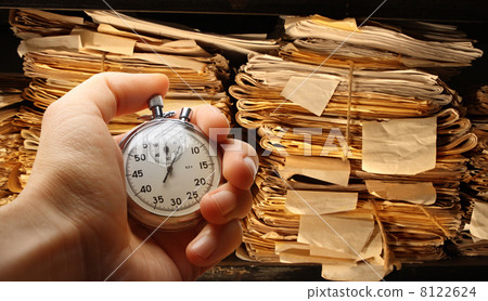 Hand with stopwatch, paper documents stacked in archive 8122624