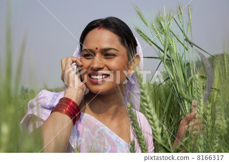 Indian female farm worker looking away while talking on mobile phone 8166317