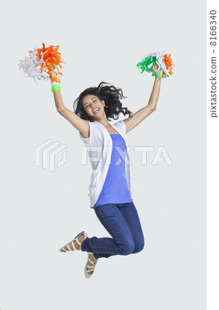 Full length of young woman jumping in mid-air with Indian tricolor pom-poms over colored background Full length of young woman jumping in mid-air with Indian tricolor pom-poms over colored background 8166340