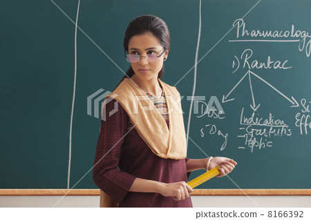 An angry female lecturer holding ruler against green board An angry female lecturer holding ruler against green board 8166392