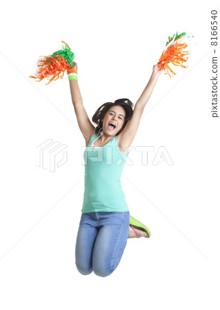 Excited young woman jumping in mid-air while holding pom poms over white background 8166540