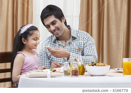Happy father feeding his cute daughter a piece of pizza at restaurant 8166778